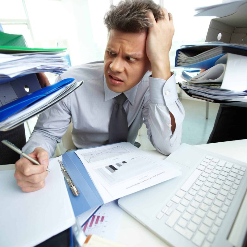 Finance medewerker zit vermoeid achter bureau met volle inbox en documenten| Finnt